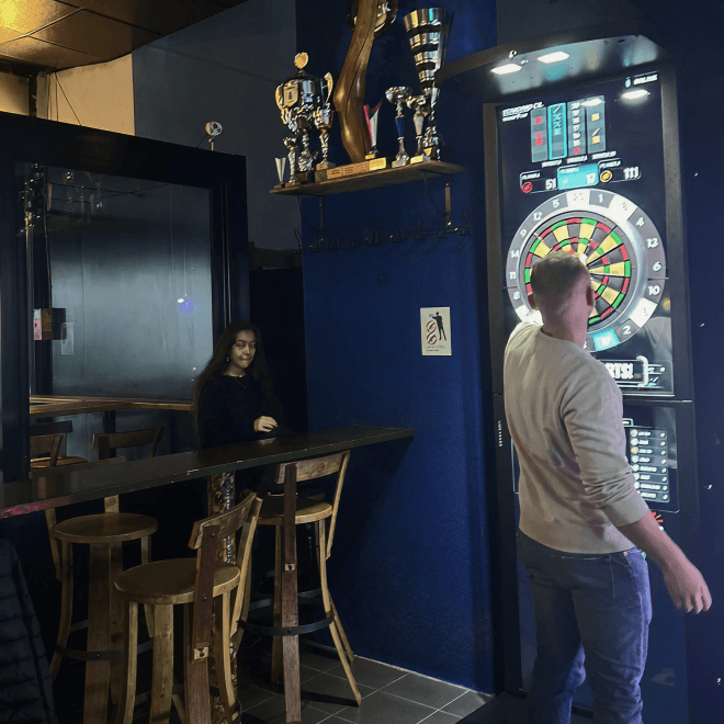 Joueur devant une machine Phoenix Dart dans un bar avec trophées